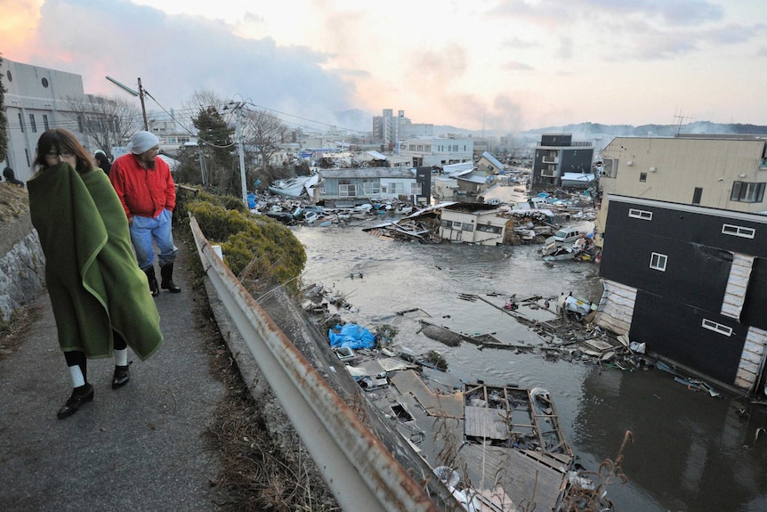 A woman wrapped in a blanket walks past a flooded Japanese city hit by a tsunami