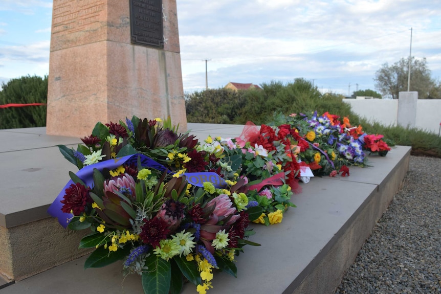 Floral wreathes laid at the base of a war memorial.