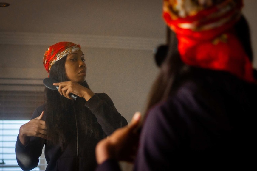 a trans woman brushing their hair in front of mirror