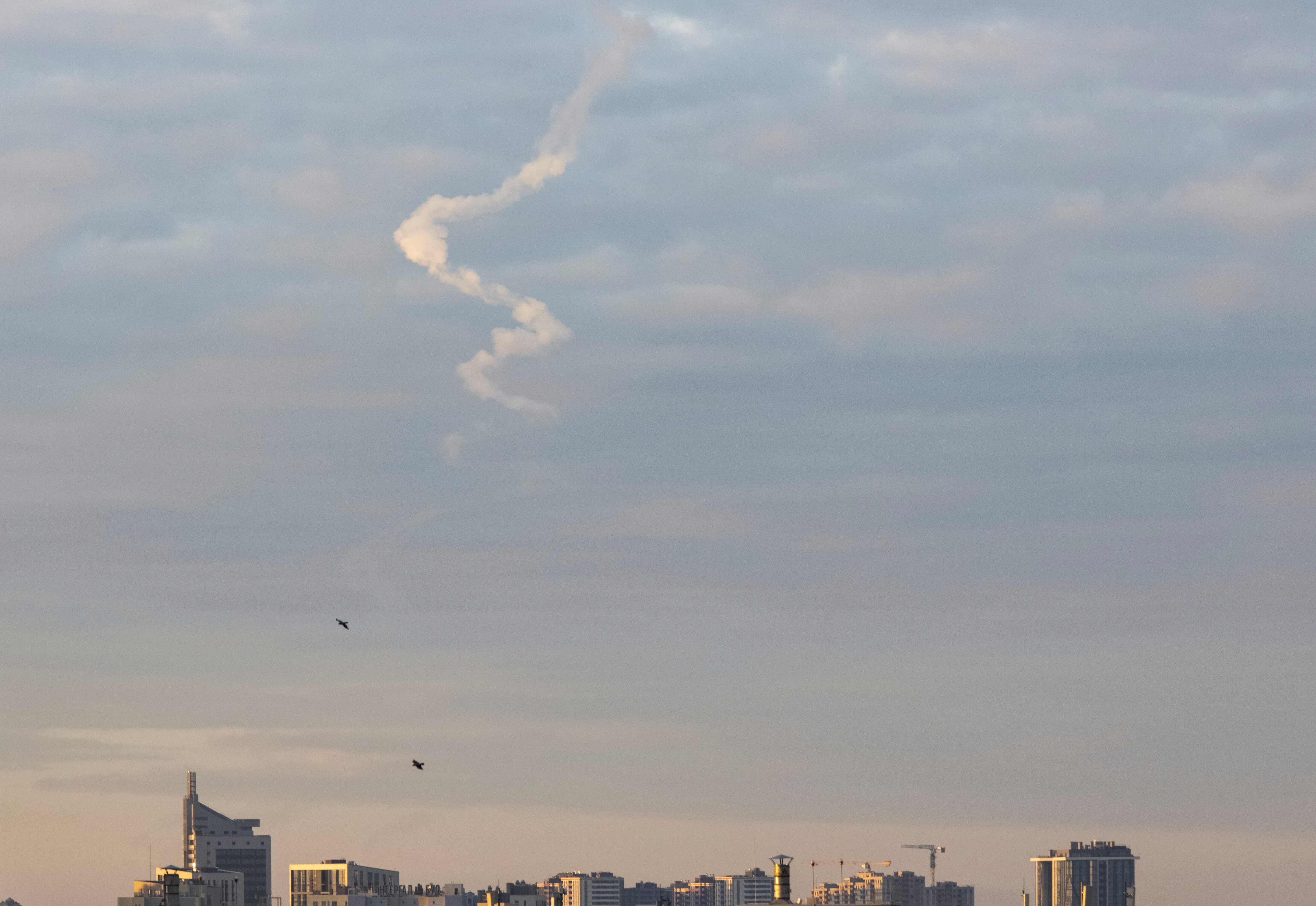 A missile trace is seen in the sky above the top of city skyline.