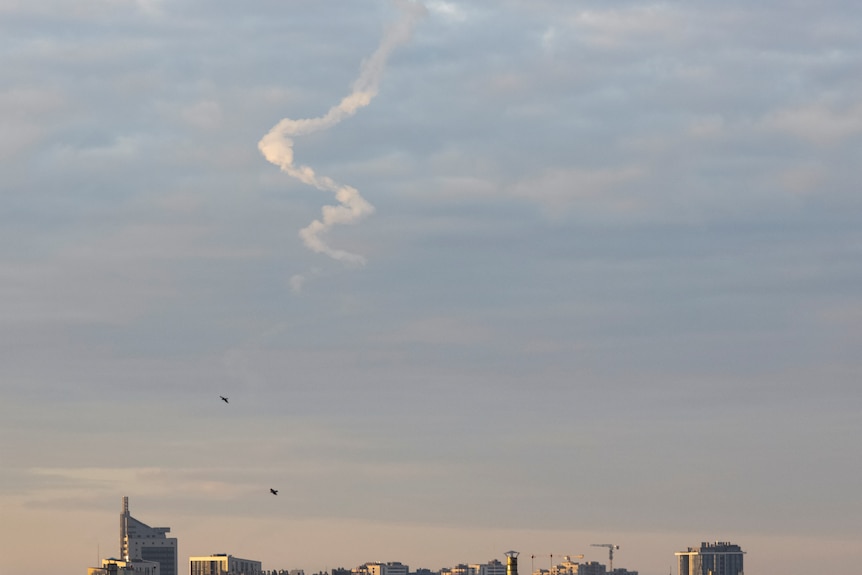 A missile trace is seen in the sky above the top of city skyline.