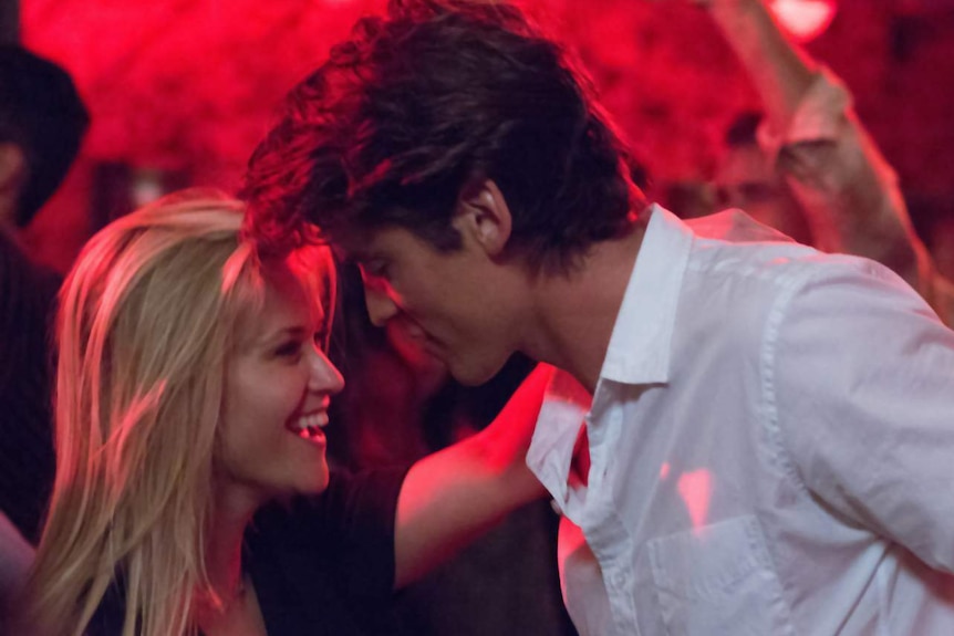 Colour still image of actors Reese Witherspoon and Pico Alexander dancing in a neon lit scene.