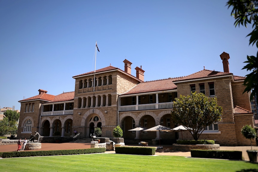 A historic three story building with arches and columns on its facade. It has a statue and green lawns in front of it.