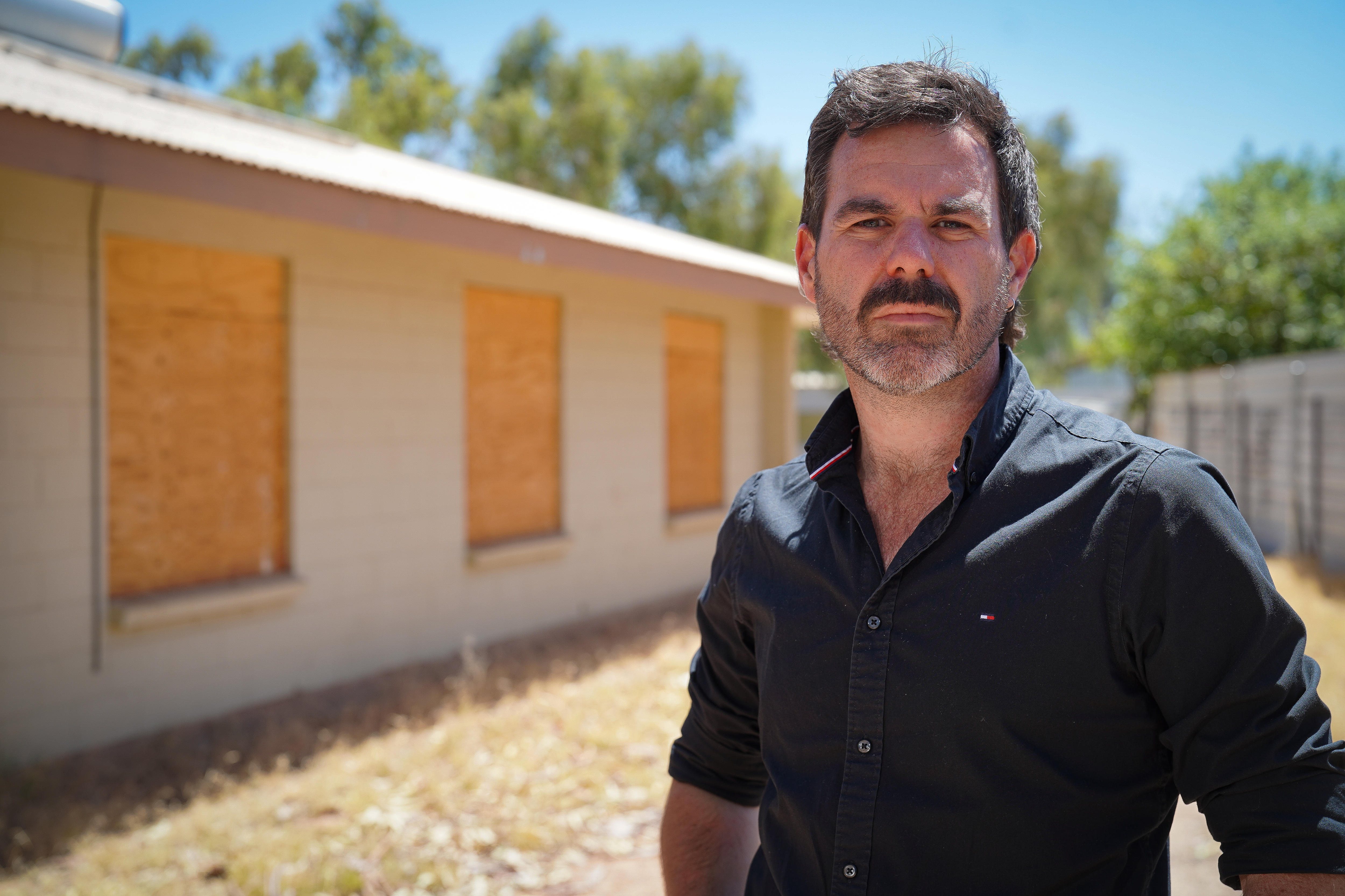 Um homem de camisa azul em frente a um prédio de habitação pública.