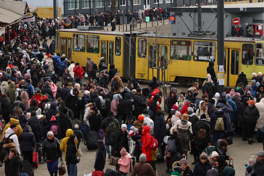 Crowds of people wait at a train station.