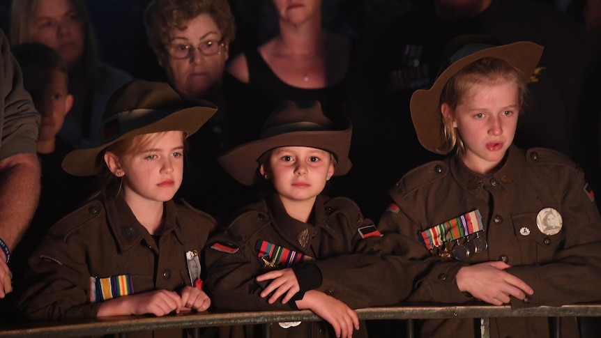 Three children wear veteran's medals, faces lit by candle light.