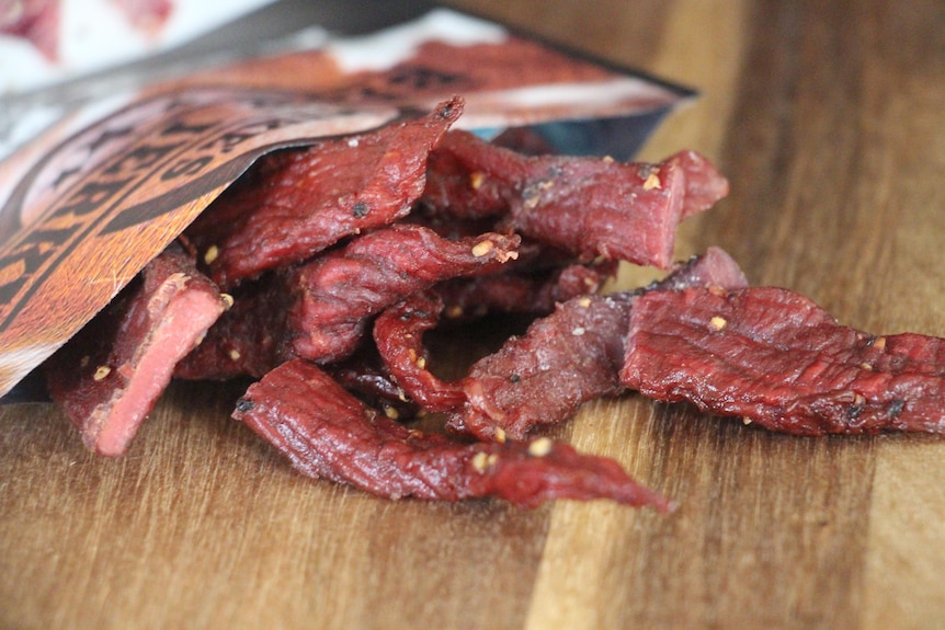 A pile of beef jerky spilling out of a packet onto a wooden board