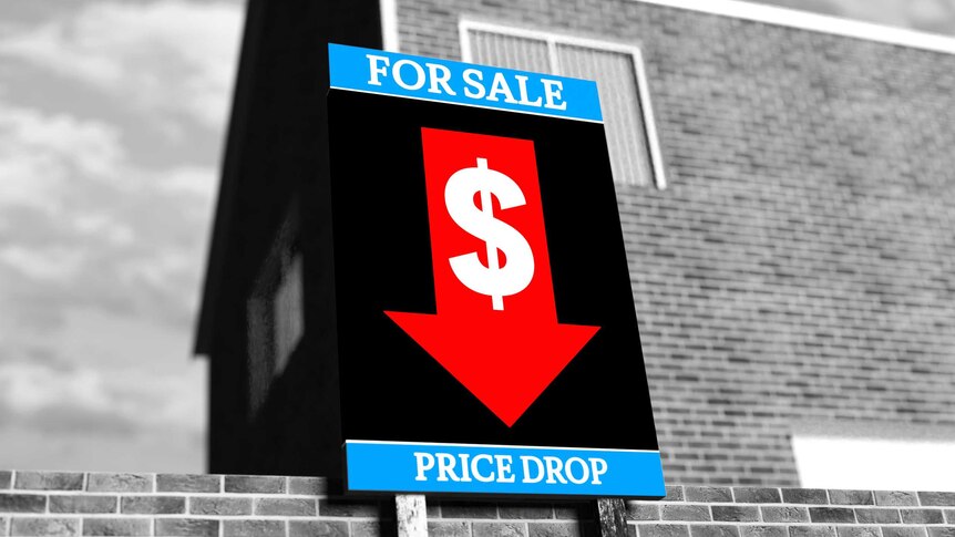 A house with a for sale sign outside, in the sign is a downward facing arrow indicating a price drop.
