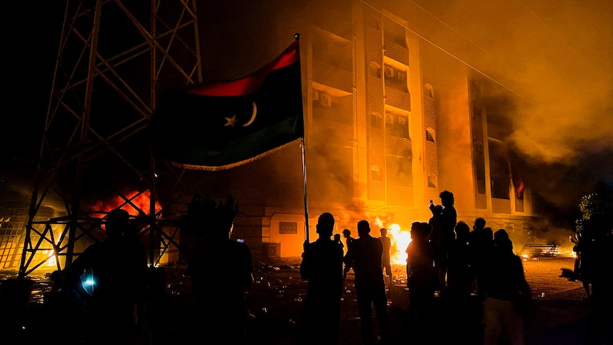 A night-time showing people silhouetted in front of a burning building.