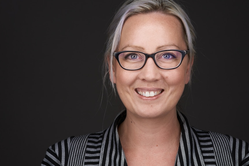 A smiling woman with blond hair tied back and wearing glasses.