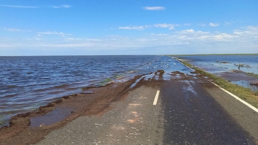 A road mostly inundated with water next to a flooded paddock.