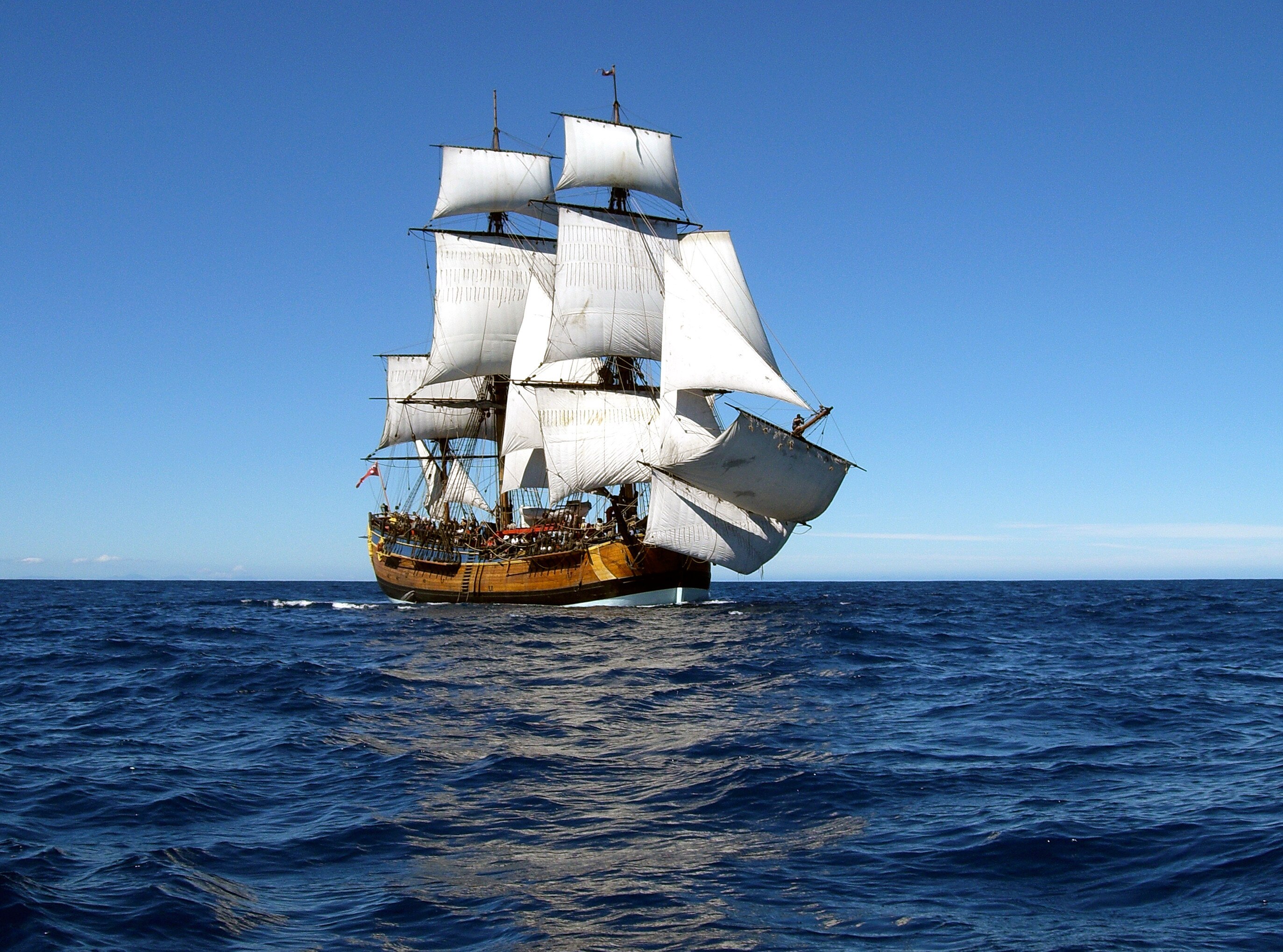 A wide photo of a replica of the Endeavour - a on old ship with many sails - at sea.