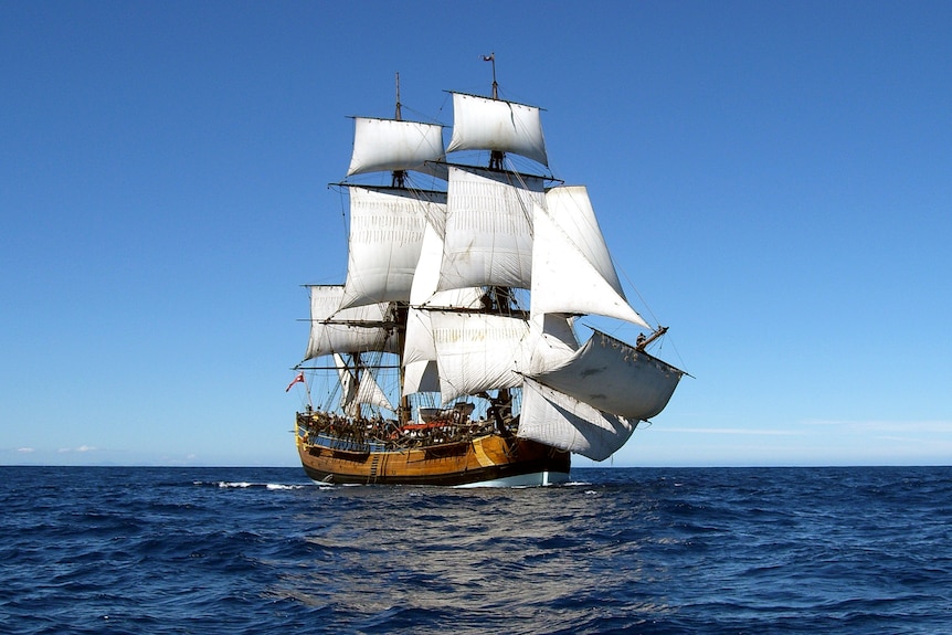 A wide photo of a replica of the Endeavour - a on old ship with many sails - at sea.