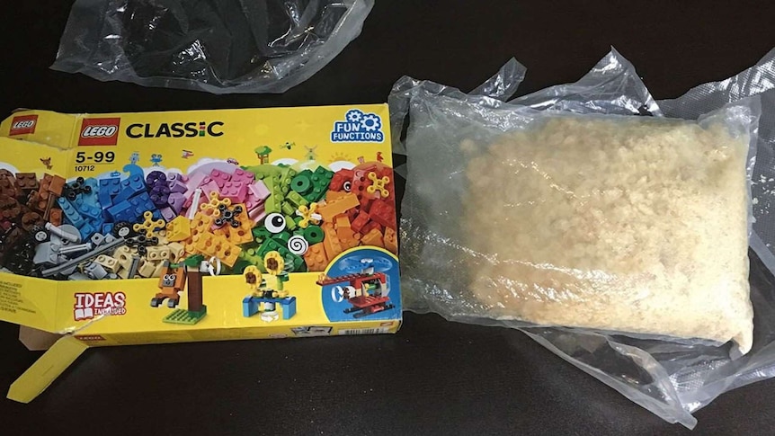 A Lego box next to a bag of a light-brown crystal substance, sealed in plastic packaging.