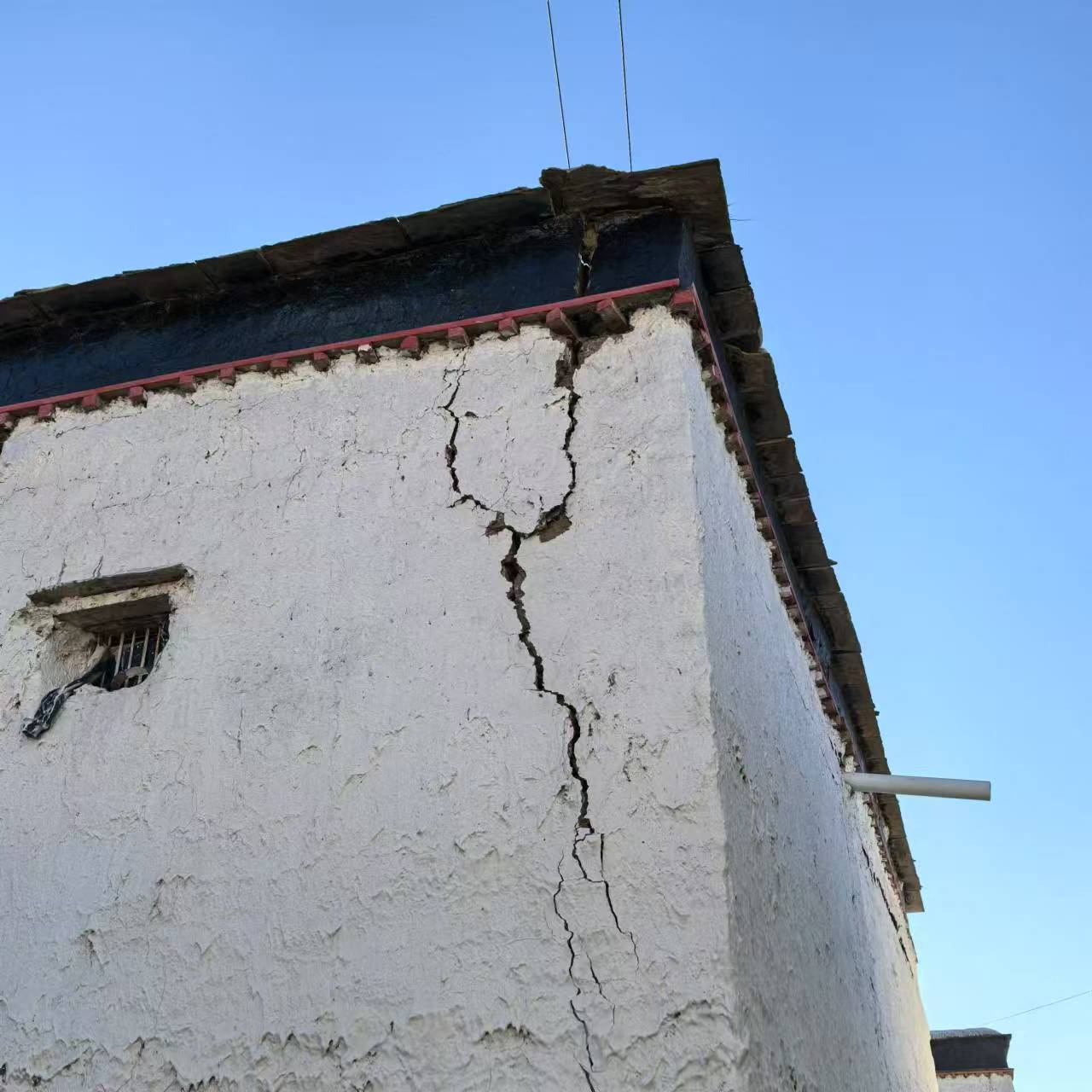 The corner of a white building with a black roof showing a large black crack spreading from the guttering into the wall