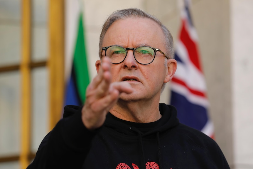 Anthony Albanese pointing towards the camera in front of Australian flags. 