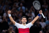 Novak Djokovic stands with his hands in the air smiling