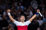 Novak Djokovic stands with his hands in the air smiling
