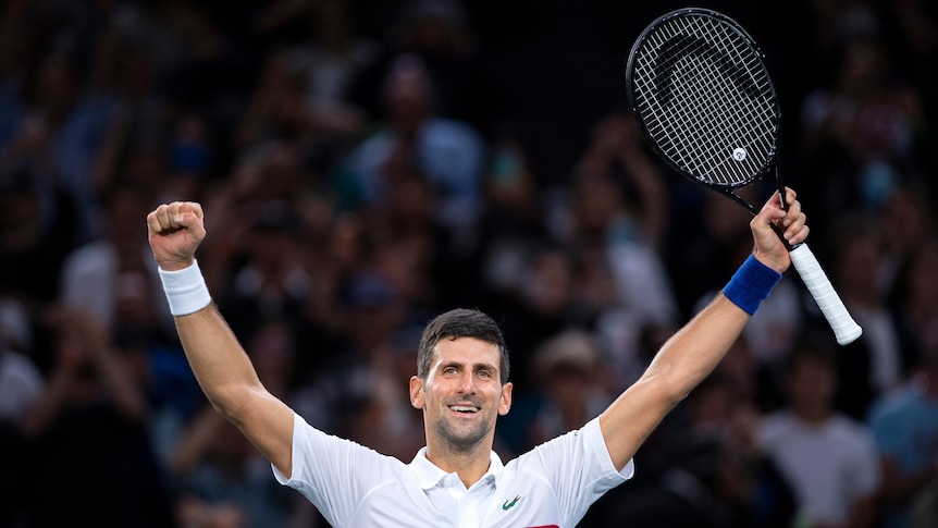 Novak Djokovic stands with his hands in the air smiling