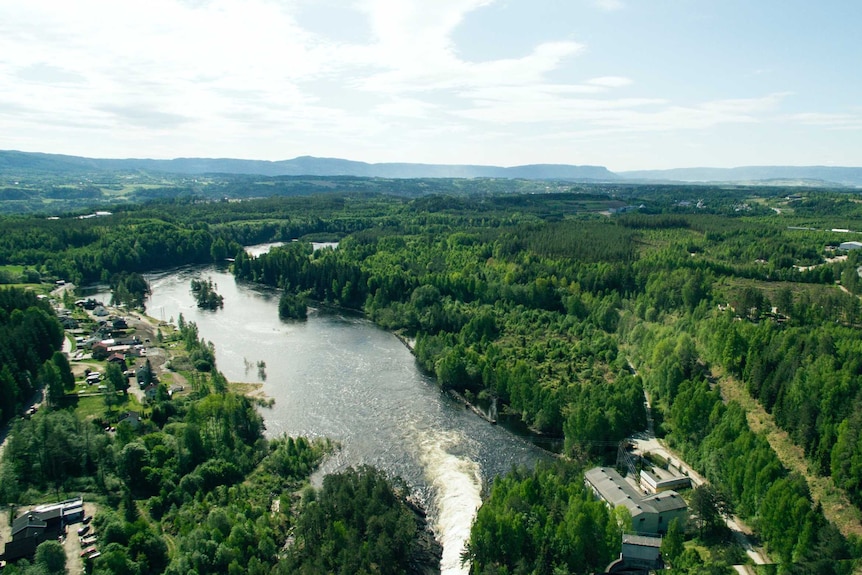 An aerial photo shows lush, green Norwegian forests beside a river driven through a narrow channel.