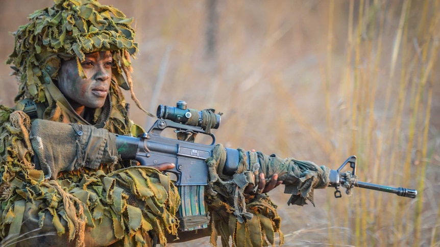 Midshot of Akashinga woman in green camouflage top and hat, holding a large gun.