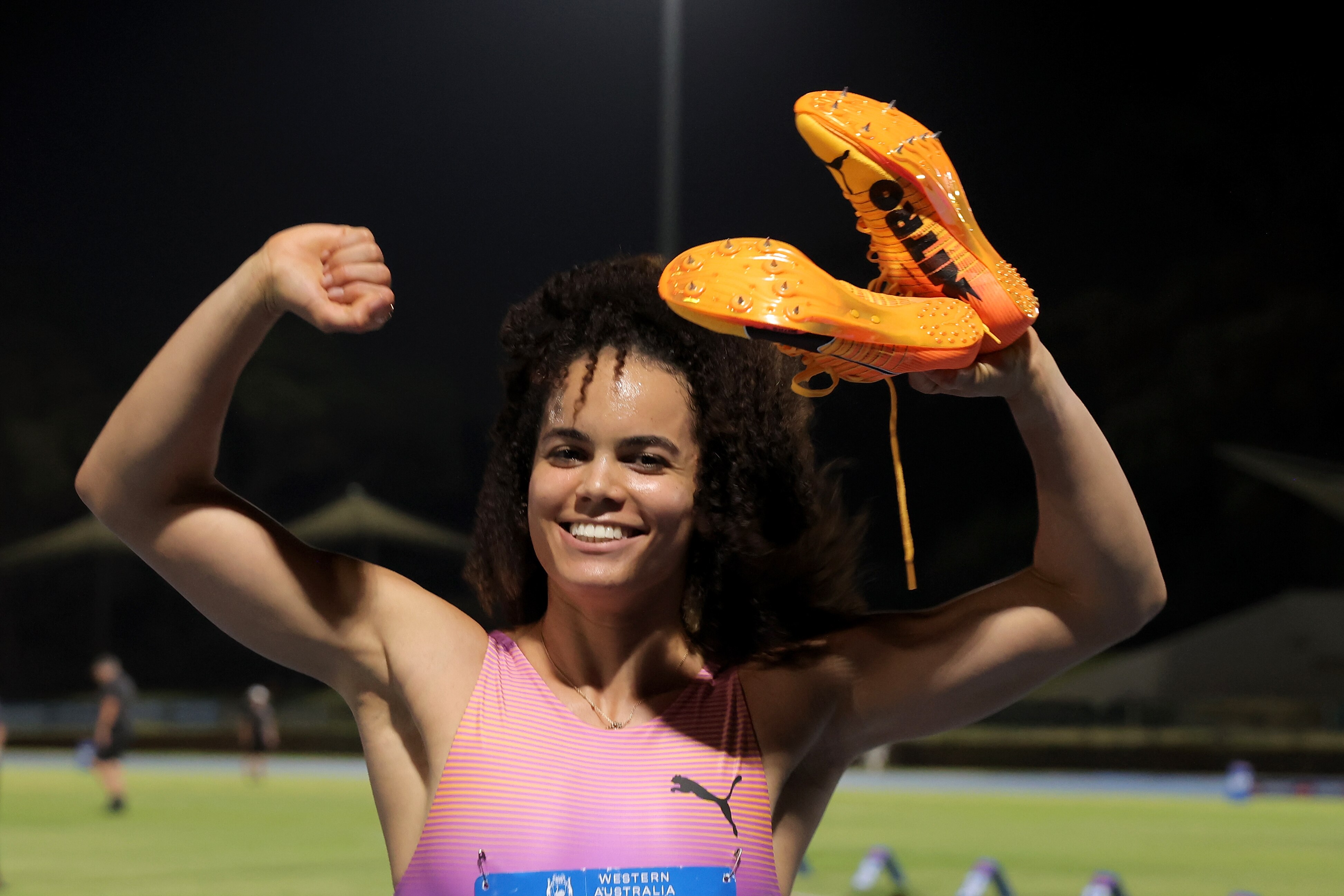 Sprinter Torrie Lewis raises her arms in victory, holding her running shoes