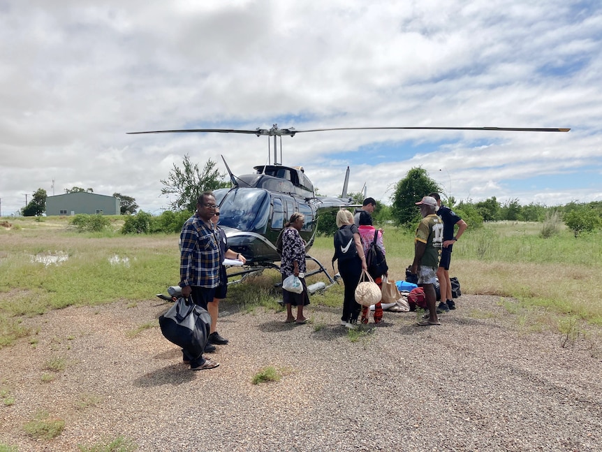 People with bags stand next to a helicopter in the outback.