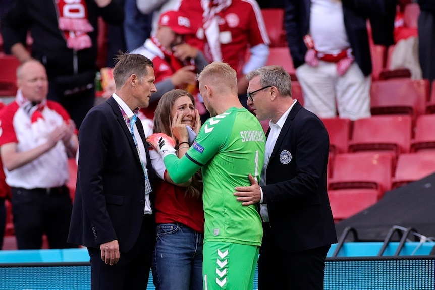 Kasper Schmeichel holds a woman, who is crying by the shoulders, flanked by two men in suits.