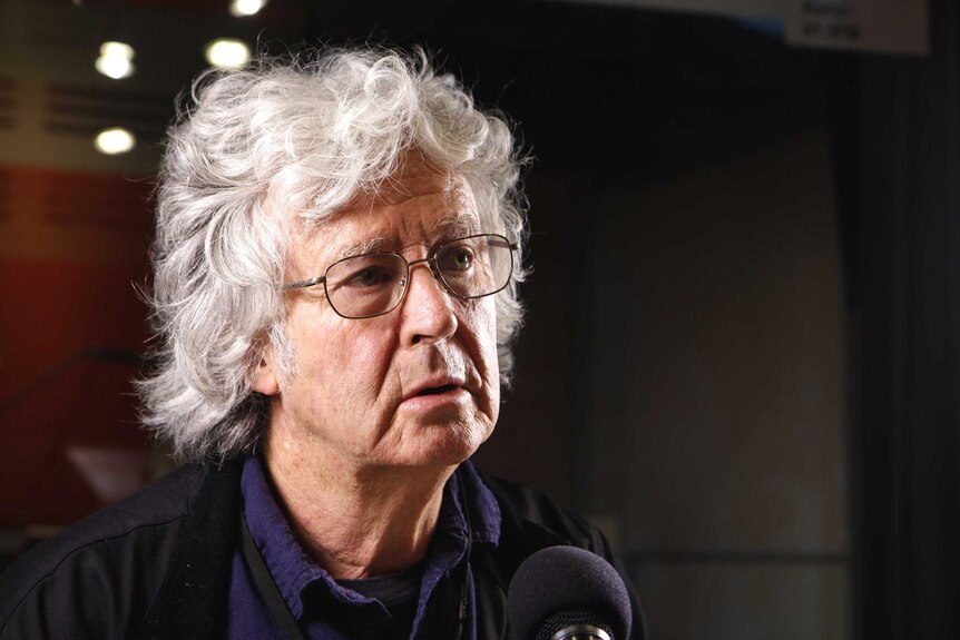 Michael Leunig looks thoughtfully to an interviewer as he sits in front of a microphone in a radio studio.