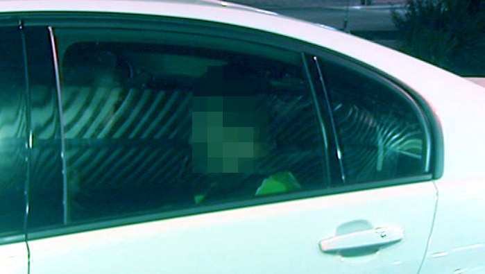 A man sitting in a white police car with his face pixellated.