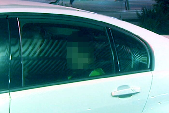 A man sitting in a white police car with his face pixellated.
