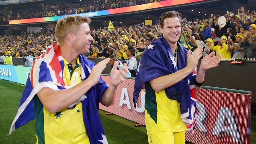 Cricketers David Warner and Steve Smith walk around the MCG with Australian flags over their shoulders.