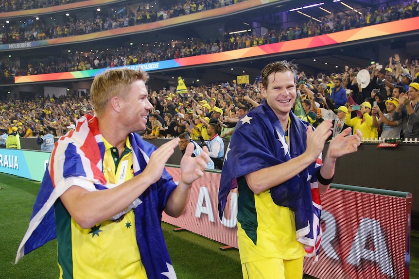 Cricketers David Warner and Steve Smith walk around the MCG with Australian flags over their shoulders.