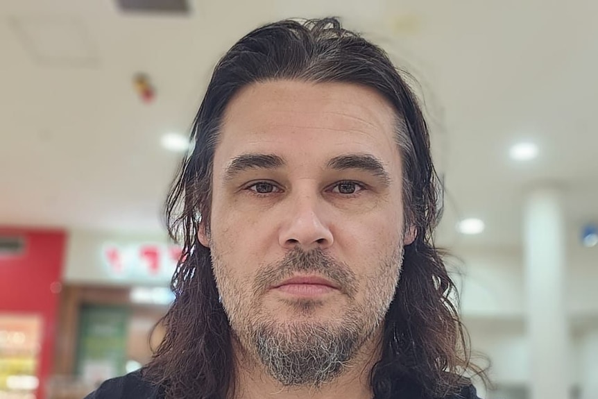 a man with long hair looks to the camera in a shopping centre
