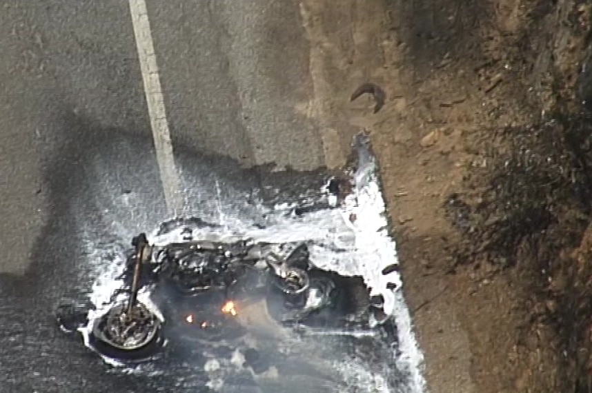 A burnt motorbike laying on the ground with water and foam doused over it.