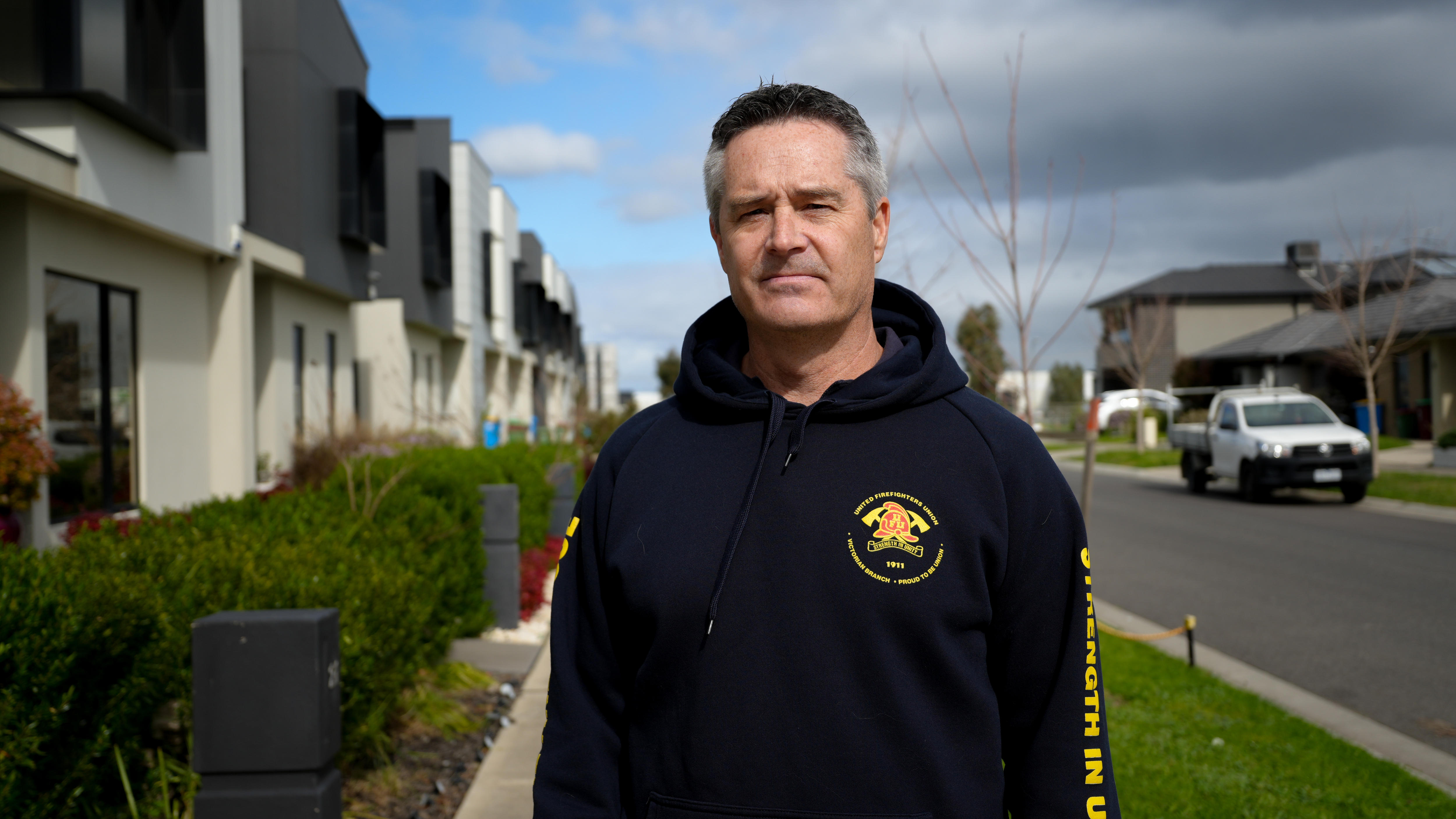 Man standing on footpath of suburban street with houses in background wearing united firefighters union jumper