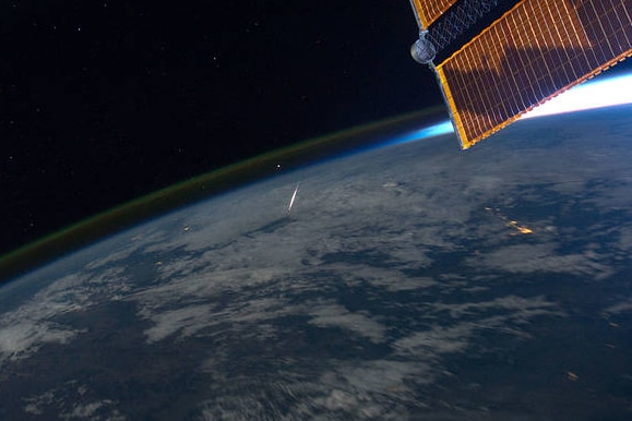 A photo from space looking towards Earth as a bright orange shooting object descends towards it 