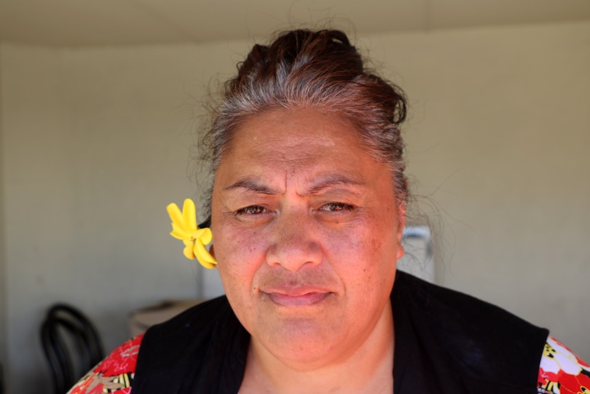 A woman with a yellow flower tucked behind her ear, in headshot.