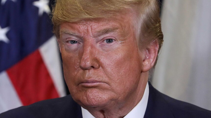 A close photo of Donald Trump's face shows the president looking serious. A US flag is in the background.