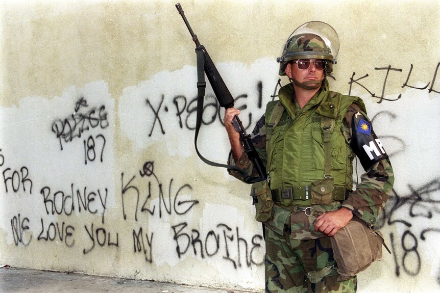 A National Guard soldier with a gun standing in front of a wall covered in graffiti