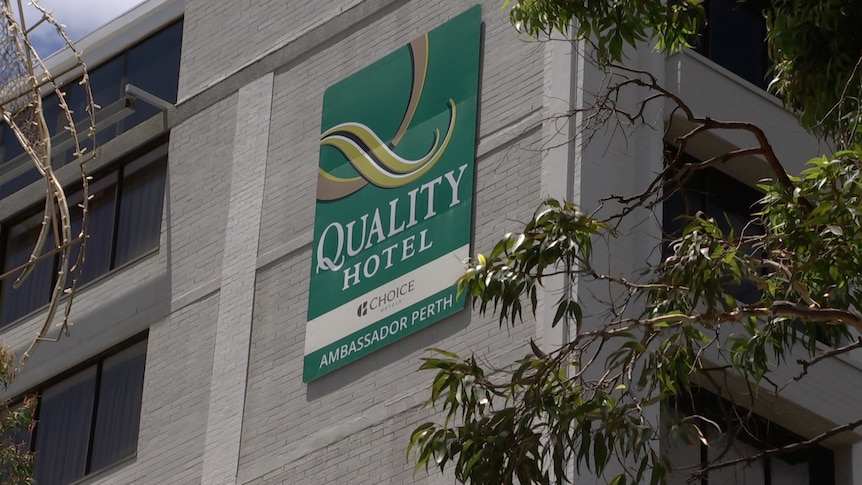 A green sign on grey building that says Quality Hotel Ambassador Perth