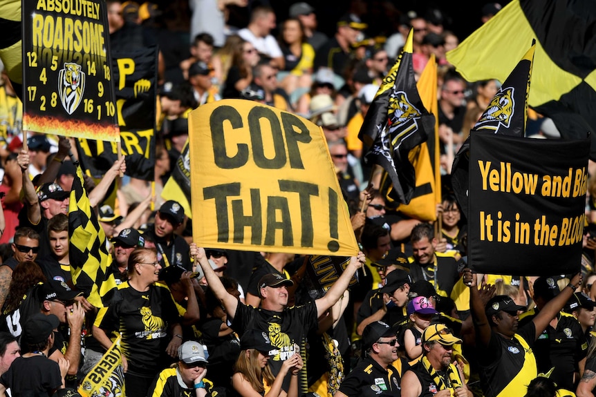 Richmond supporters hold up banners and wave flags at an AFL match.
