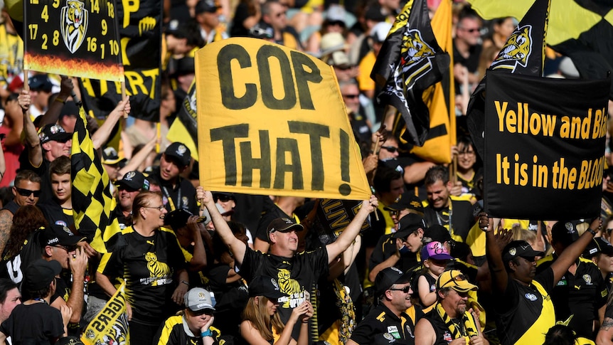 Richmond supporters hold up banners and wave flags at an AFL match.