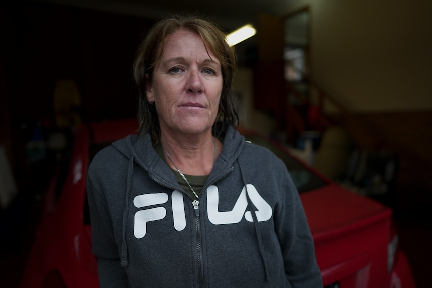 A woman wearing a hoodie looks into the camera with a serious expression on her face.