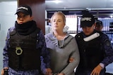 Cassandra Sainsbury wears handcuffs and street clothes and is held by two uniformed guards as she walks through a court building