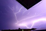 Lightning strikes across a purple sky, seen looking up from under an awning.