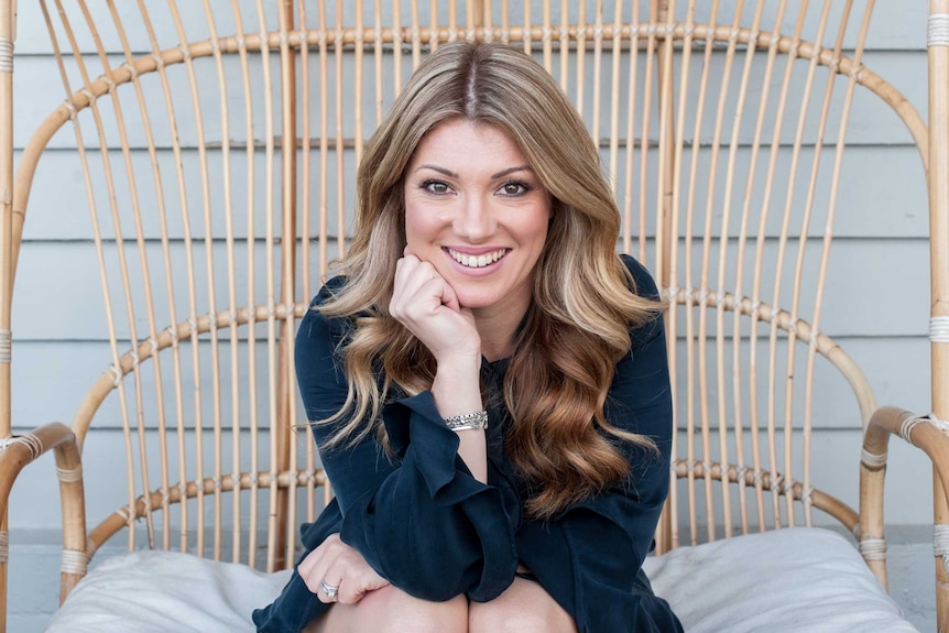 Natalie Kringoudis sitting in a cane chair and smiling at the camera.