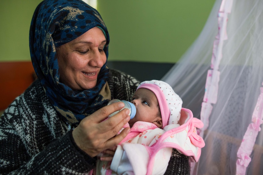 Mahboba holds a small baby and feeds her with a bottle. 