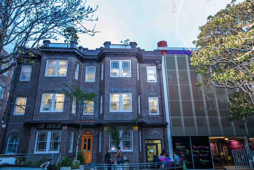 People mill about outside a three-storey brick building