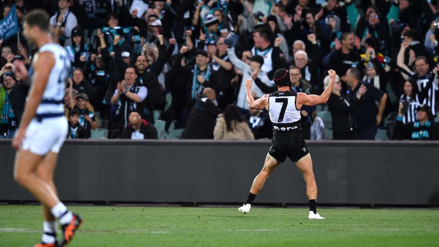 An AFL footballer stands in front of a cheering crowd and pumps his fists in celebration.